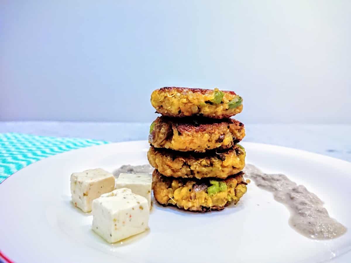 quinoa patties arranged vertically on a plate with coconut walnut sauce and feta cheese cubes